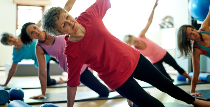 Quatro pessoas fazendo exercícios de alongamento em ambiente fechado | Atividade física para a osteoporose