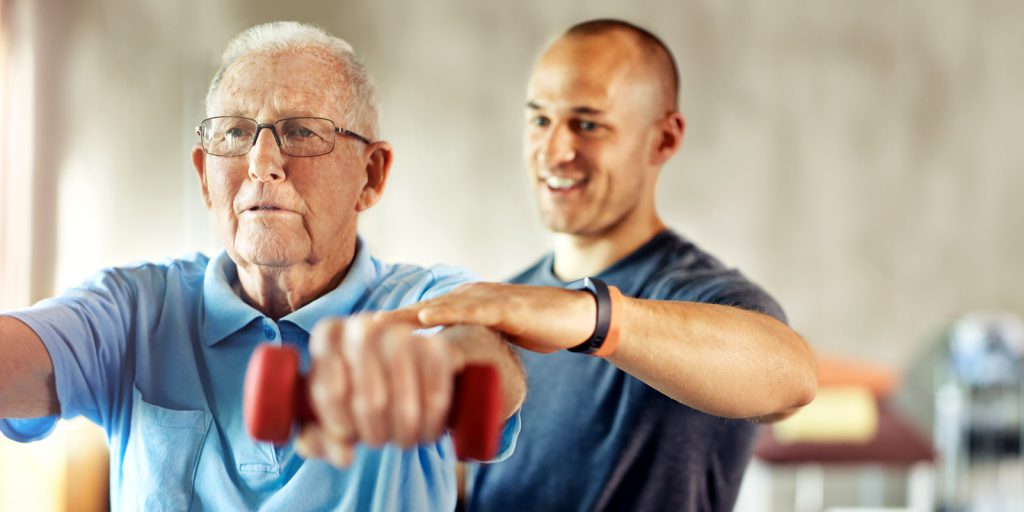 Idoso faz exercícios com haltere junto com instrutor | Tratamento da osteoporose