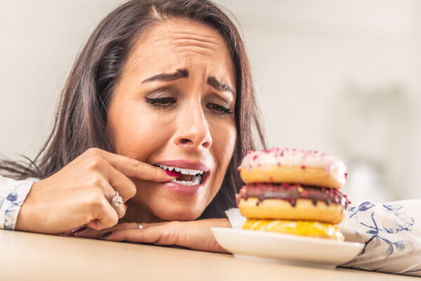 Female desperately trying to resist donuts, biting her finger.